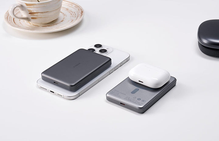 Torrasのダークグレーポータブル電源が白いiPhoneの上に置かれ、シルバーの電源には白いAirPodsケースがのっている。背景にコーヒーカップを置いたシンプルな構成