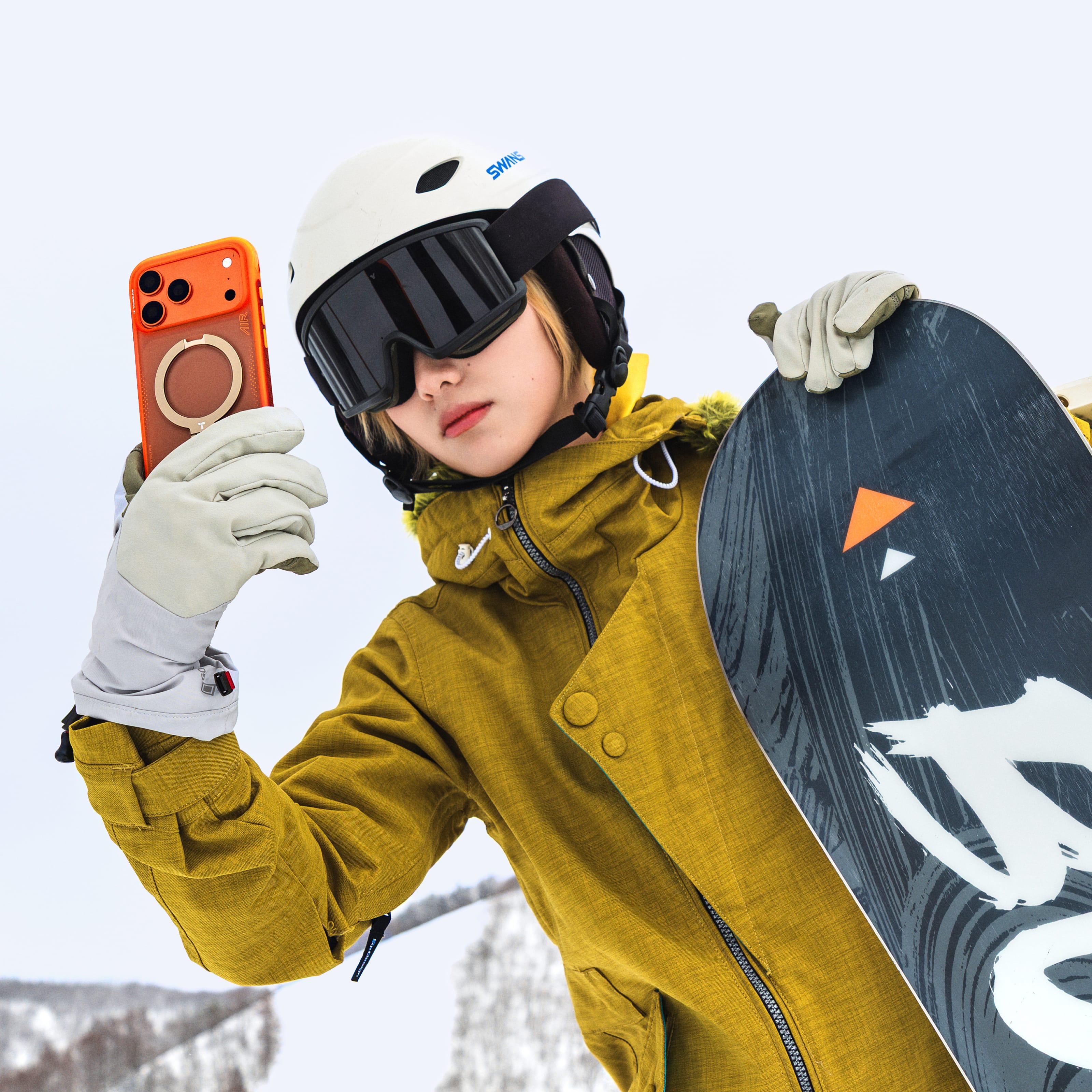 TORRAS Ostand Q3 Air ケース iPhone 18 Pro/Pro Max 対応、雪山でスノーボードウェア姿の男性がオレンジのケースを手に持つウィンタースポーツシーン。