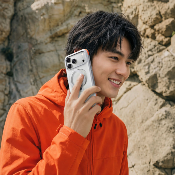 TORRAS Ostand Q3 Rugg ケース iPhone 18 Pro/Pro Max 対応、屋外でダークブルーのケースを手に持つ黒キャップ姿の男性ポートレート。